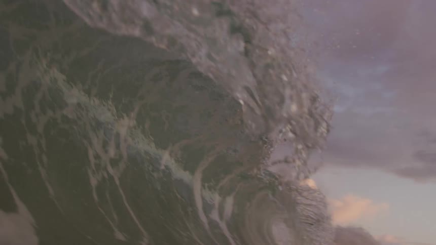 Large wave swells up under a storm cloud and crashes allowing view of sky through translucent sheet of water