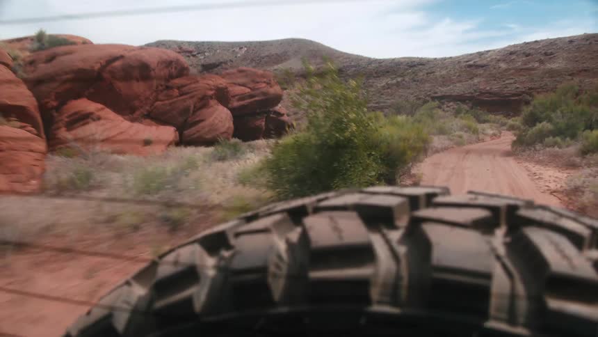 A vehicle drives down a dirt road through a canyon