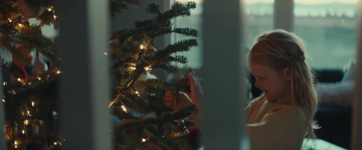 Girl smiles while hanging ornament on christmas tree as brother walks away