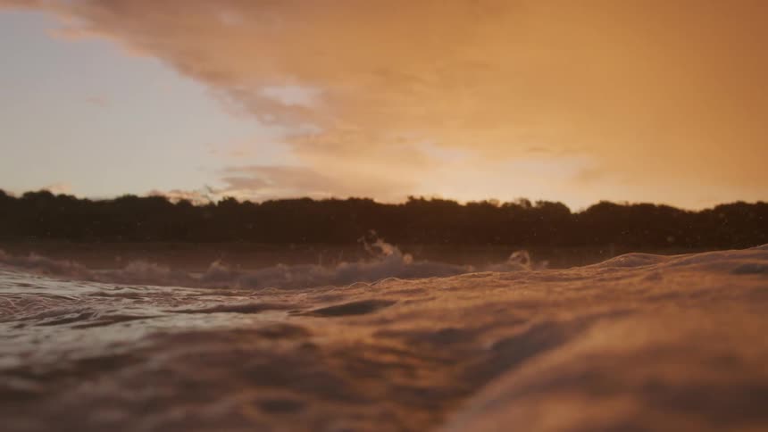 Rough water waves are splashing high in the air under a dark orange sky as the color reflects on the water
