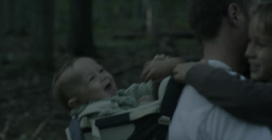 A toddler plays with his little brother while being carried by their father