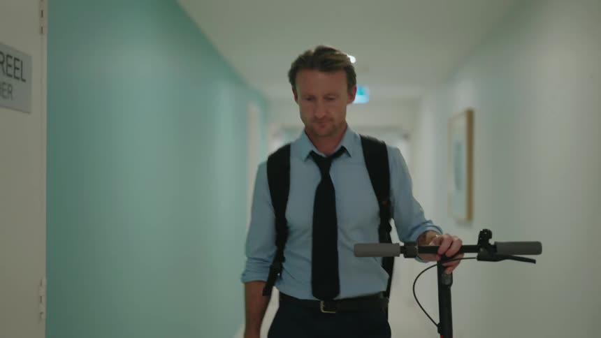 Man guides e scooter down hallway checking his smartphone before he stops to summon the elevator