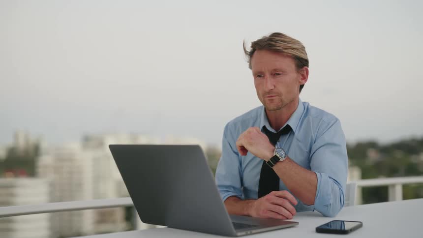 A man works on his laptop while sitting on a patio outside