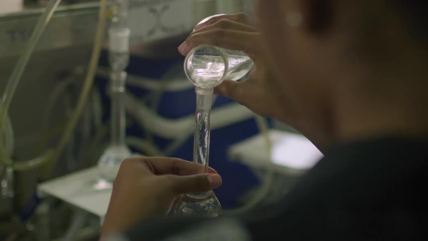 A woman is standing in a room holding a vase and pouring water into it from another glass container