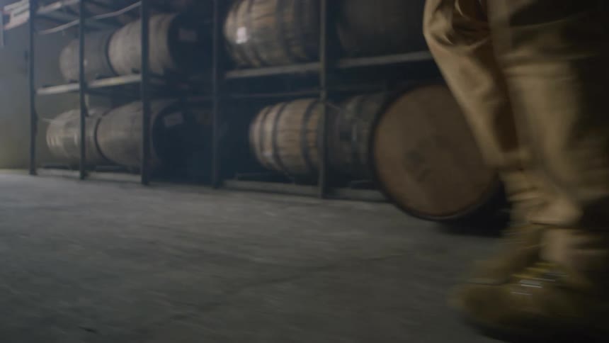 A person walks through a warehouse filled with shelves of barrels during the day