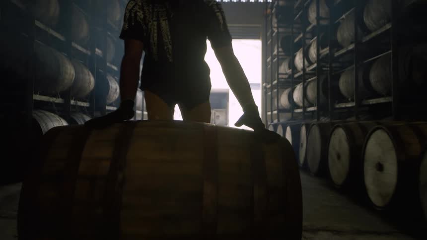 Man rolls keg along ground between warehouse shelving full of kegs