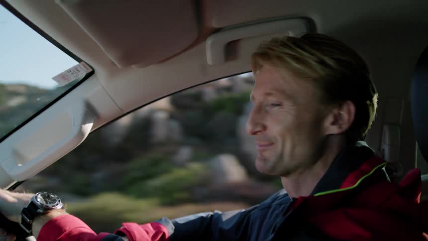 A man has a smile on his face as he is talking to someone as he drives his automobile
