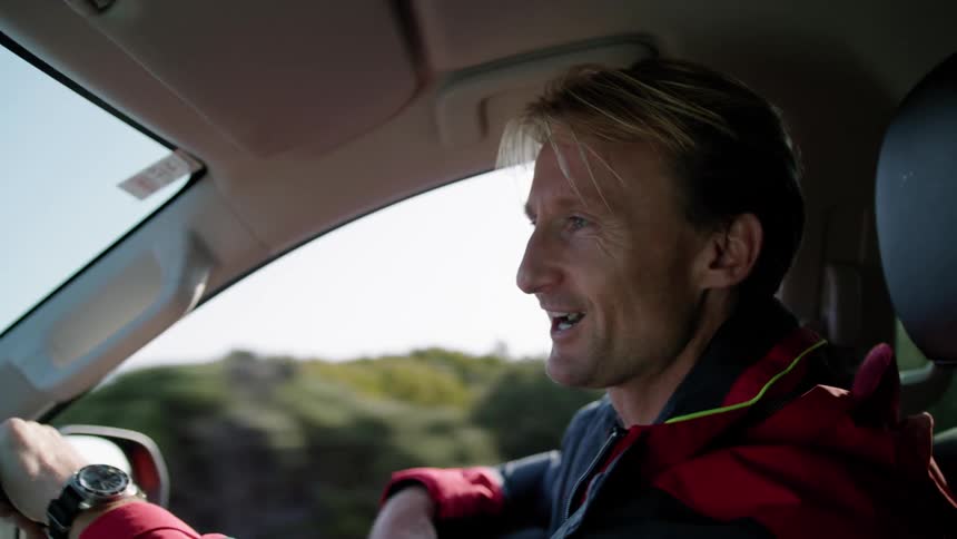 A man drives a car through the countryside while talking to a passenger