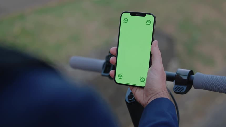 A man is standing outside holding a cell phone with a green screen