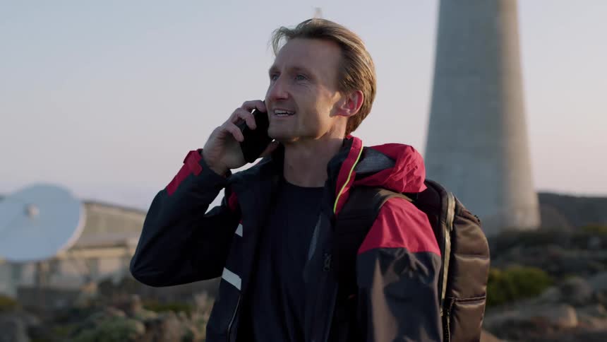 A man is talking on his cell phone in front of large satellite dish