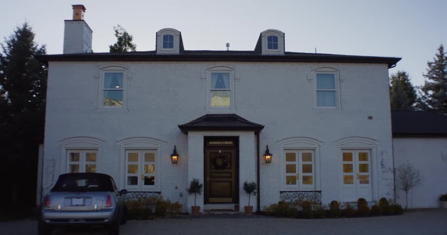 Car sits parked near large house with christmas wreath on wooden door