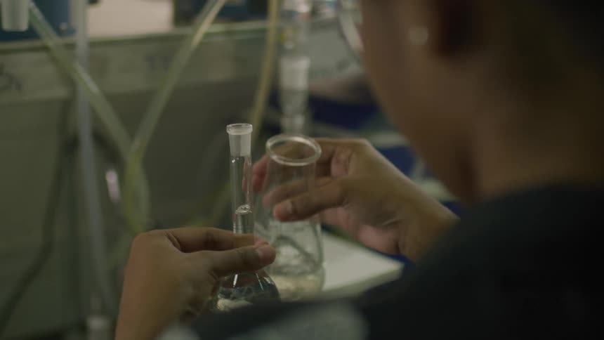 A woman is standing inside a lab pouring clear liquid into a beaker from a glass container