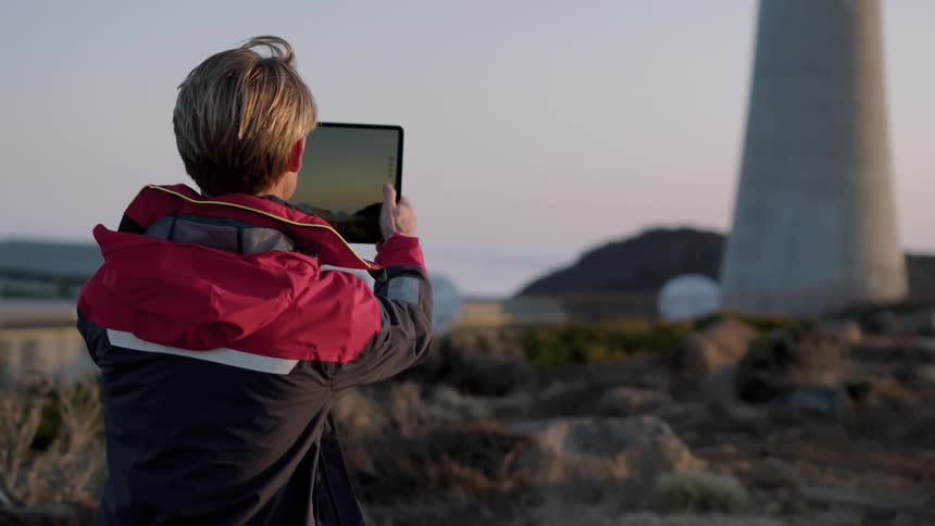 A man turns on his tablet and takes a picture of the landscape and a large tower