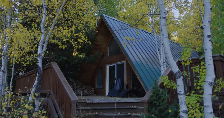 A house in the woods with chairs on the porch is surrounded by birch trees with leaves in fall colors