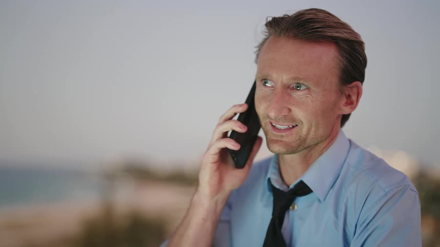 Man in light blue shirt and tie gets a phone call while typing on laptop keyboard sitting at desk