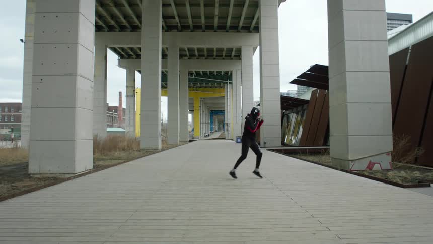 Kickboxer shadow boxes under overpass near building with factory in the distance