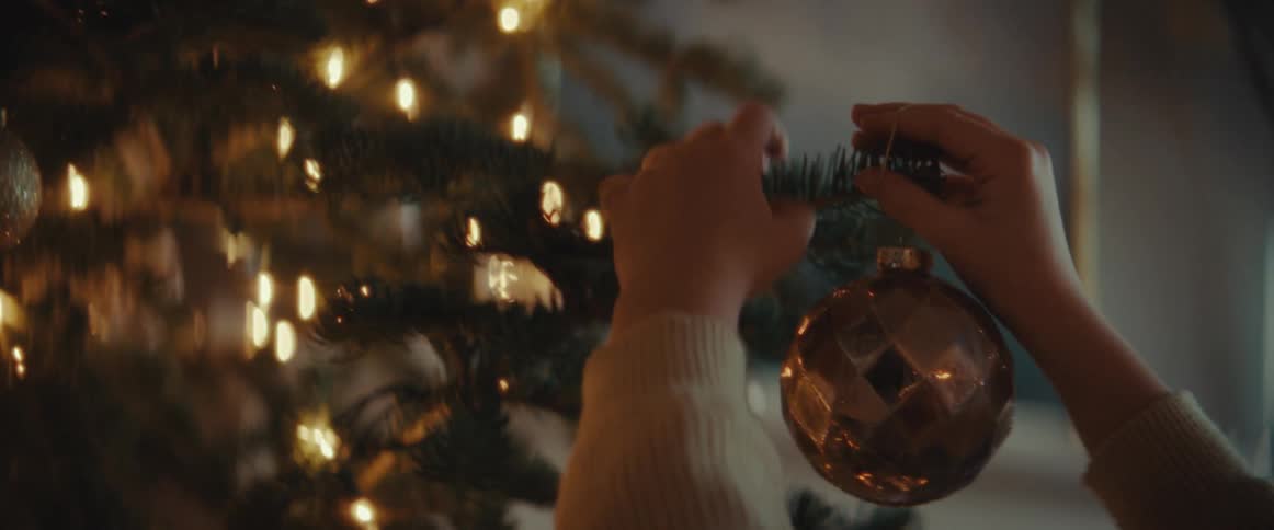 A child is reaching up and holding a branch on the christmas tree and hanging a decoration on it