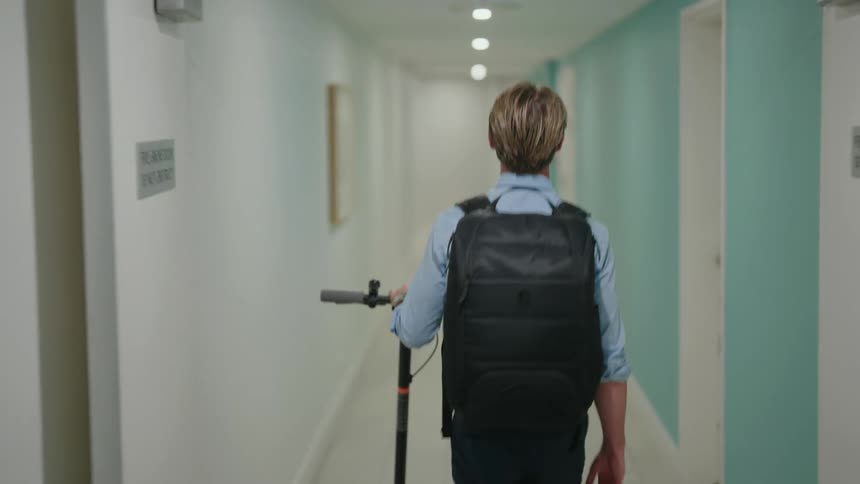 A man is carrying a scooter down the corridor