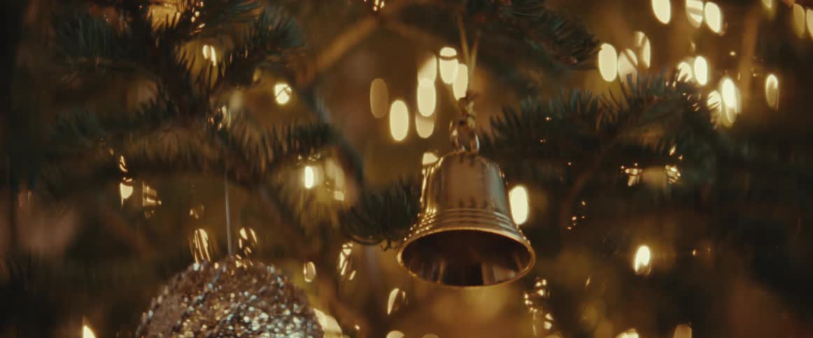 Someone wearing a sweater is hanging a bell on a christmas tree