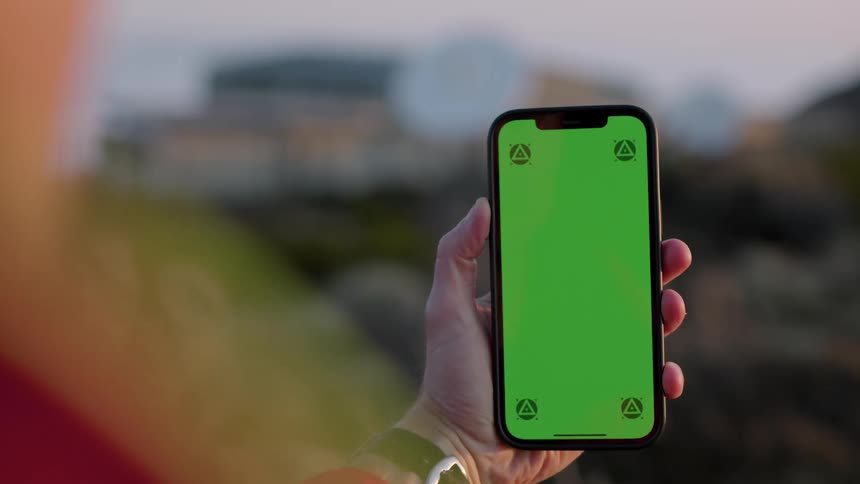 A person looks at the screen of a their smartphone while standing outdoors in the evening