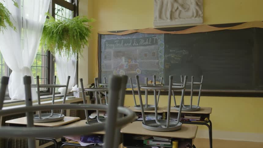 Stools placed upside down on desks in an empty classroom during the day