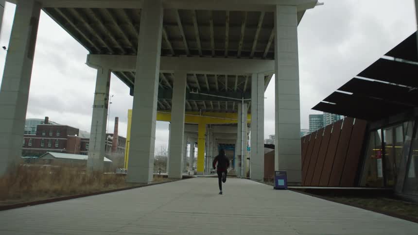 A jogger runs beneath a large bridge in a metropolis on a cloudy day