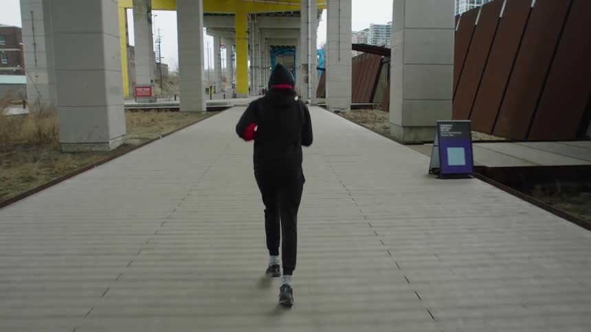 A woman runs on a paved trail under a bridge