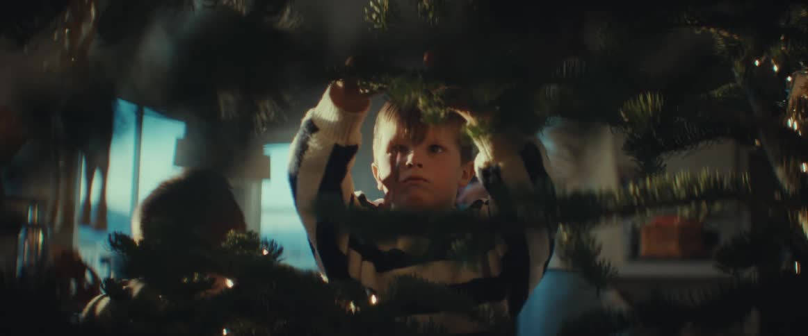 Boy with sweater decorates christmas tree in room