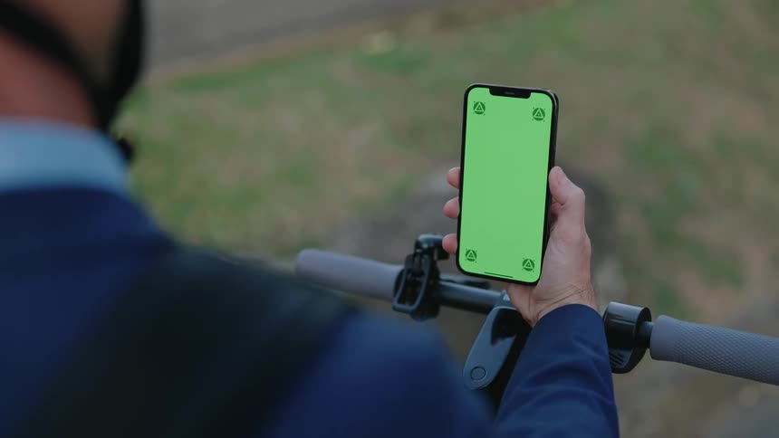 Man in dark blue suit and helmet stands on electric scooter using smartphone