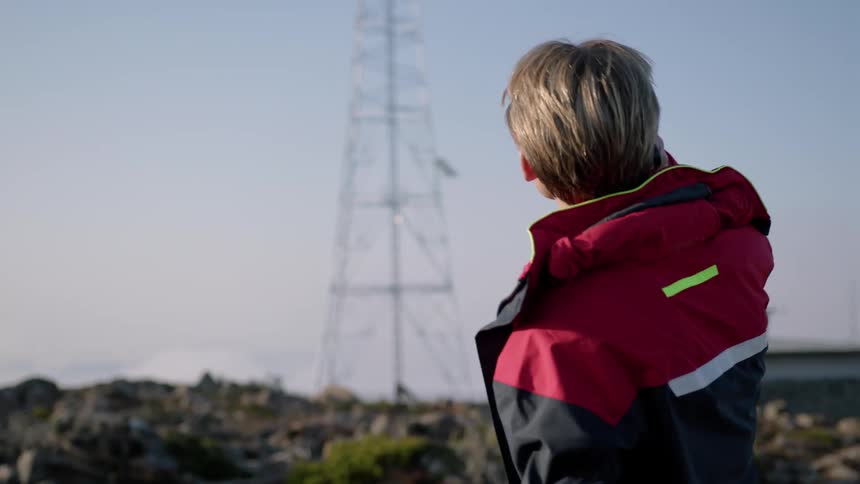 Middle aged blonde man wearing black and red coat answers incoming phone call on smartphone