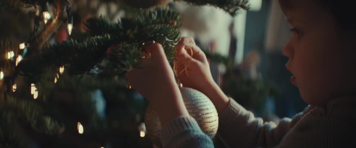 A boy hangs an ornament on the christmas tree
