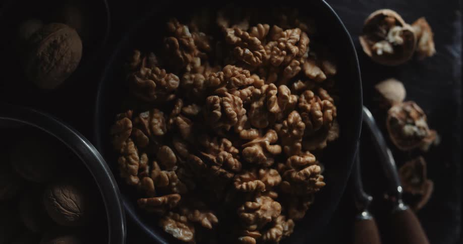 A dark bowl is filled with shelled walnuts