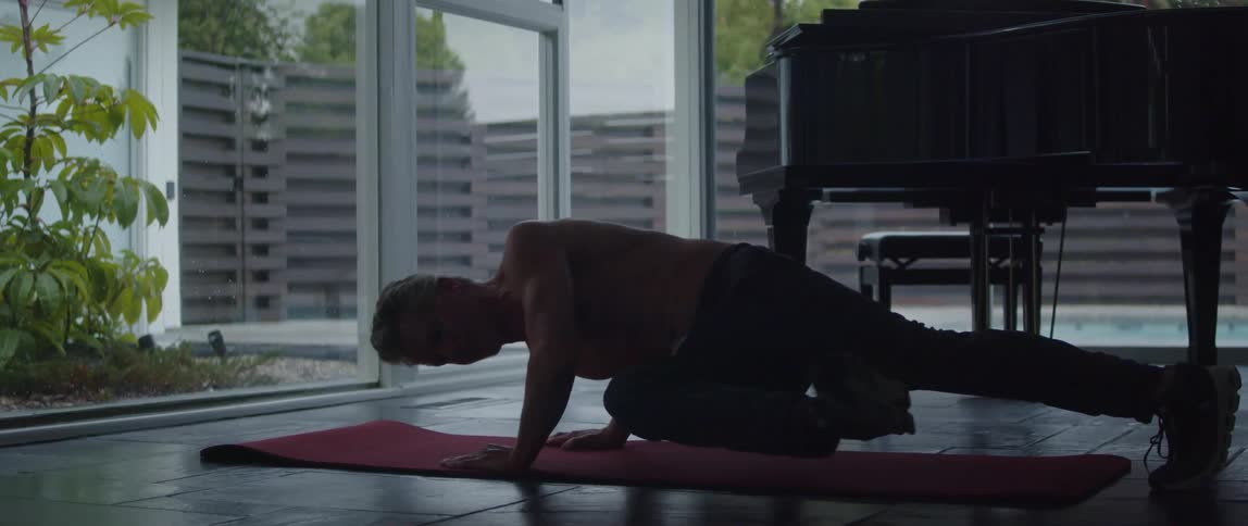 A man is on the floor doing exercises on an exercise mat near windows