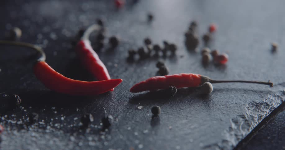 Chili peppers and whole peppercorns sit on a slate platter