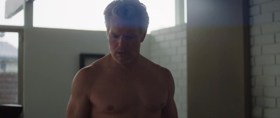 Older bare chested man looks around with shocked expression