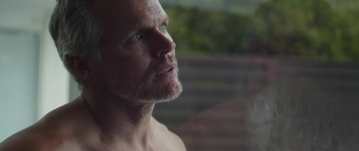 White haired man leans against reflective glass while looking out