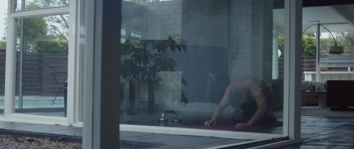 Windows on both sides of house allow view of trees as man moves through yoga stretches