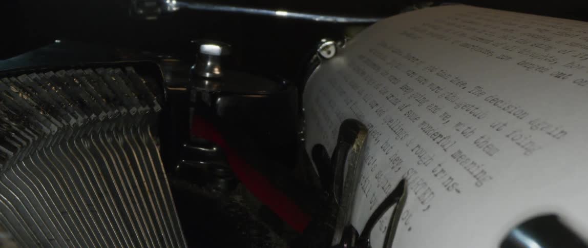 The type bars of an old typewriter are hitting the ribbon as the paper moves and text is written
