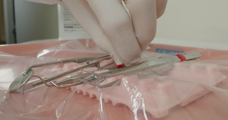 A dentist chooses a tool from a plastic covered tray