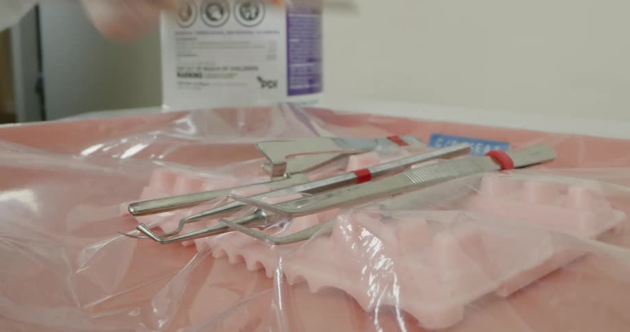 A dentists instruments are lying on a plastic sheet and a hand picks up one of them