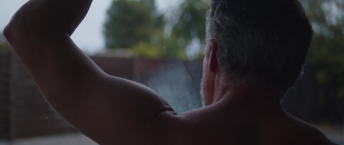 Muscular and topless man leans against the window after working out