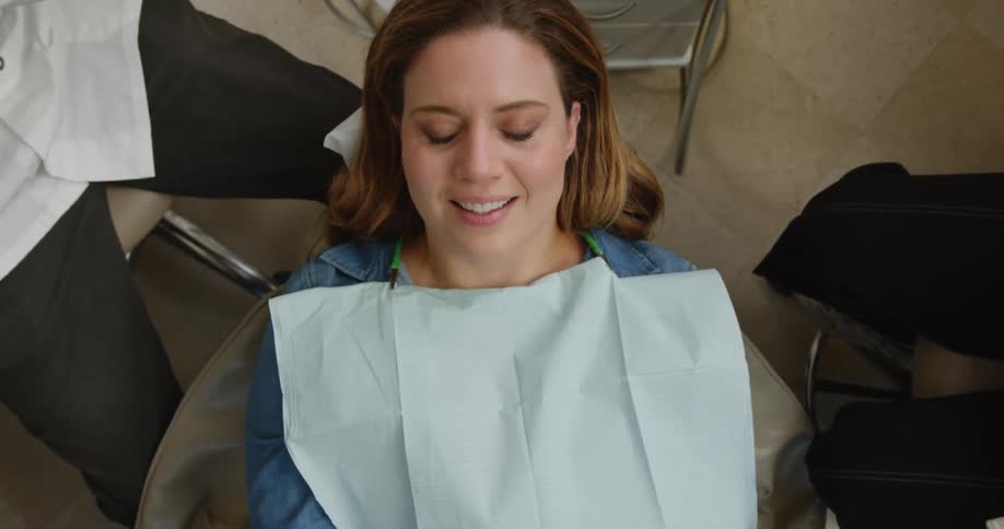 A woman leans back in a dentists chair and smiles at the dentist and assistant as they hold their instruments