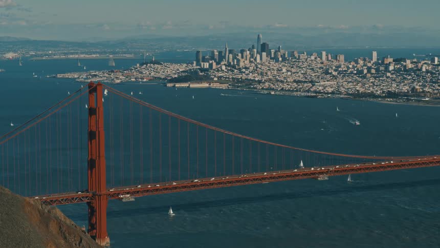 Traffic flows across golden gate bridge as boats sail through water with city skyline in the distance