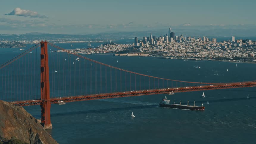 Freighter passes under busy suspension bridge with foggy city in the background