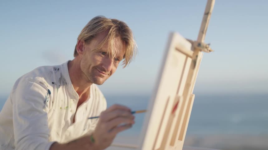 Blonde man with white shirt paints on canvas outdoors