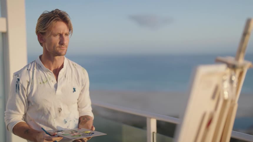 A man is standing outdoors while painting on a canvas