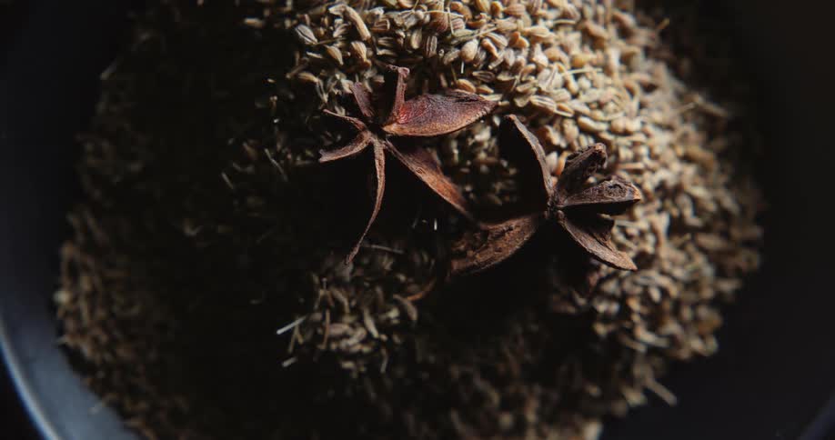 Star anise sits on top of pile of spices in black bowl