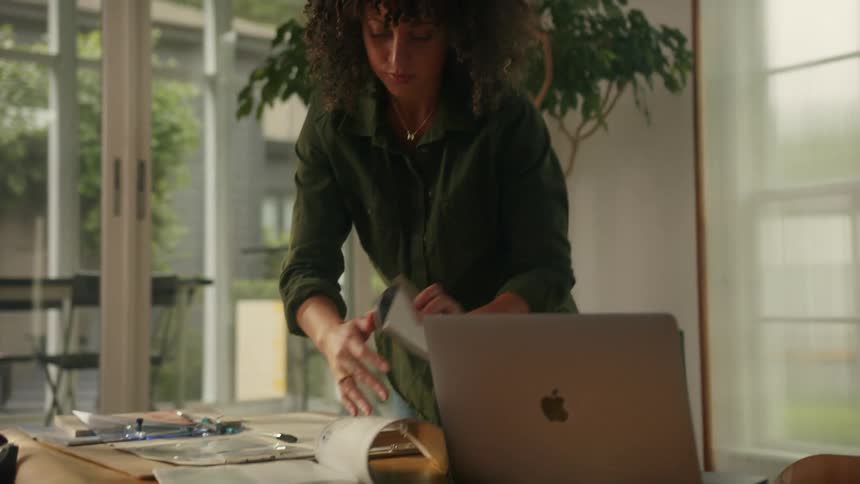 A woman in an office flips open a book and starts to write