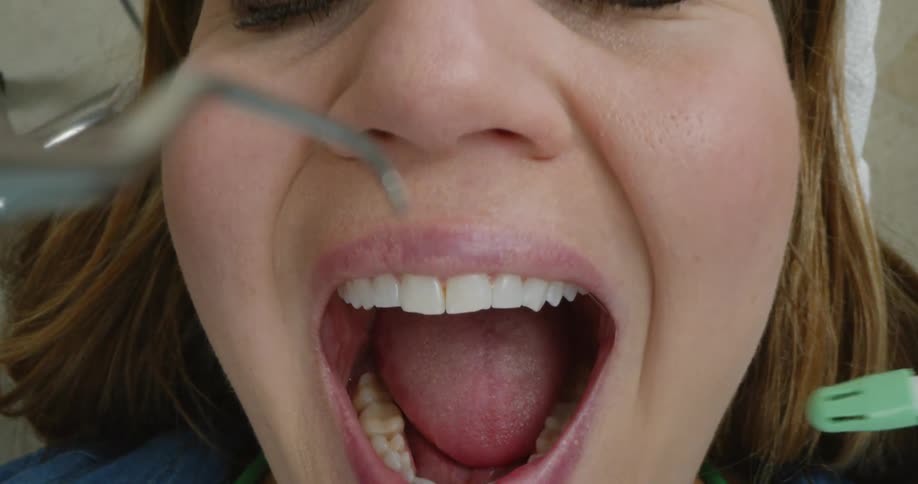 A woman lies in a dental chair and opens her mouth as dental equipment is put in her mouth