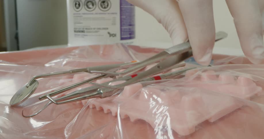 Dentistry professional wearing gloves sets tweezers down next to other dental instruments